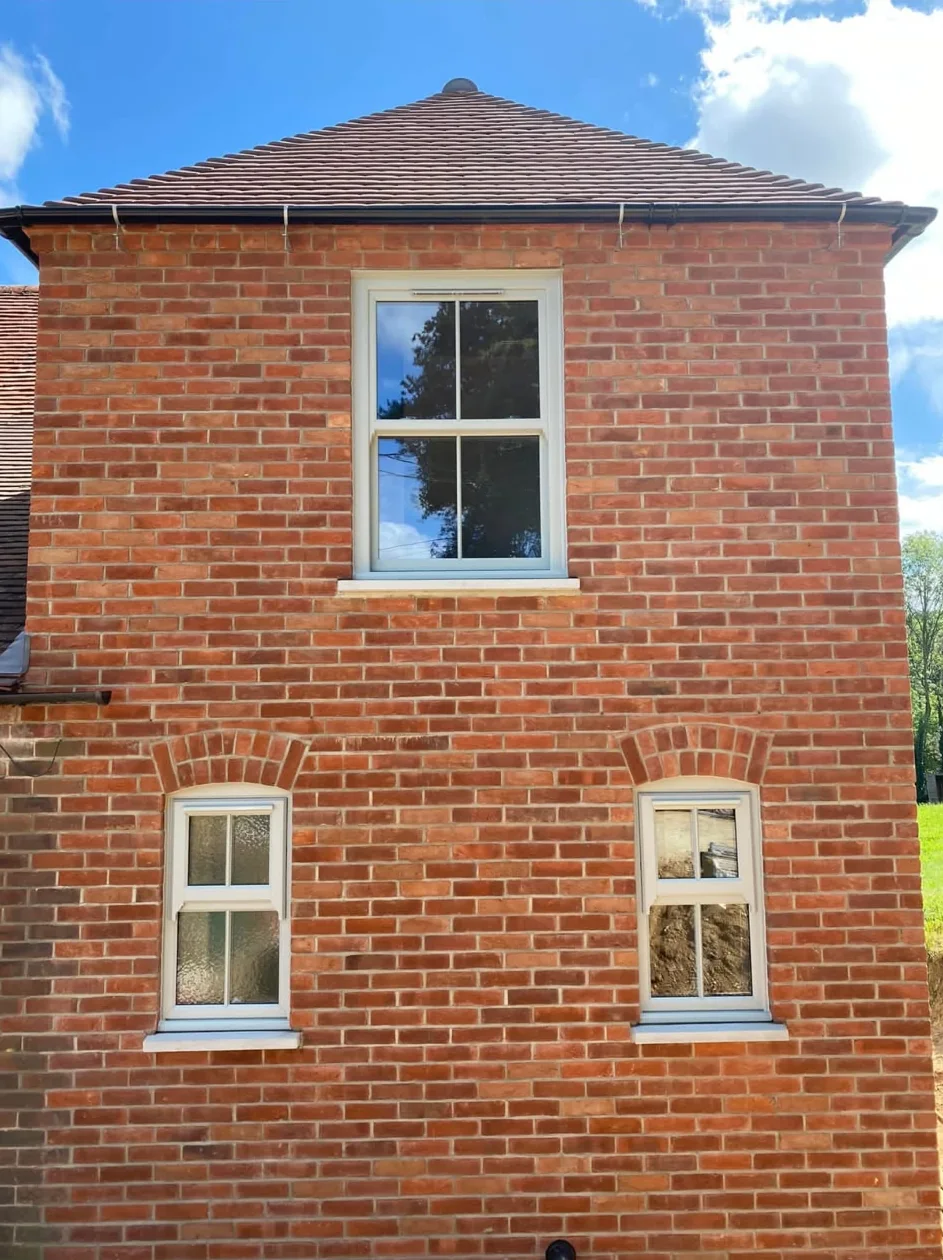 Three white sash-style windows in a red-brick gable wall under a tiled roof